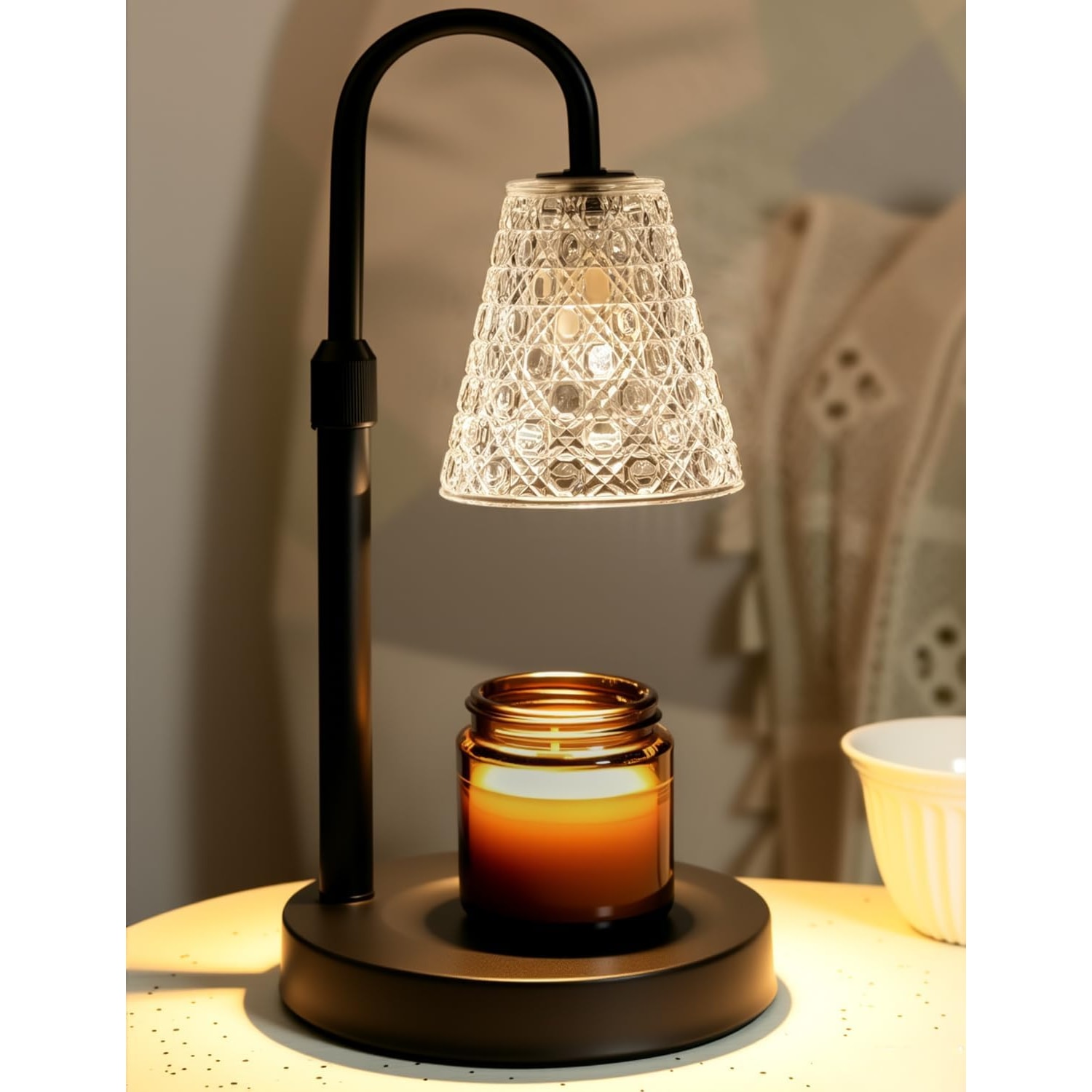 Black candle warmer lamp with a textured glass shade lit above an amber jar candle on a bedside table