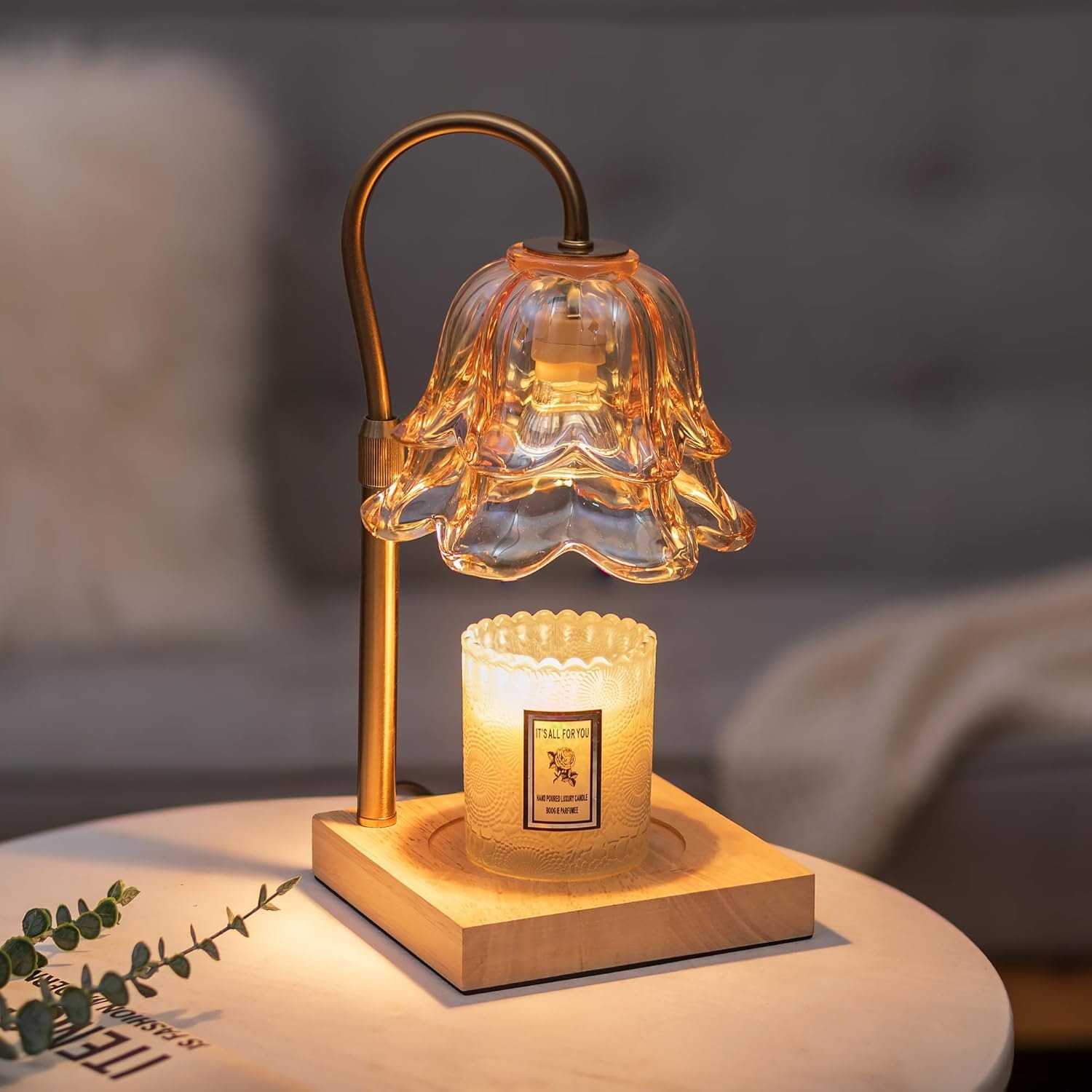 Gold flower-shaped candle warmer lamp lit above a jar candle on a marble table with eucalyptus stems