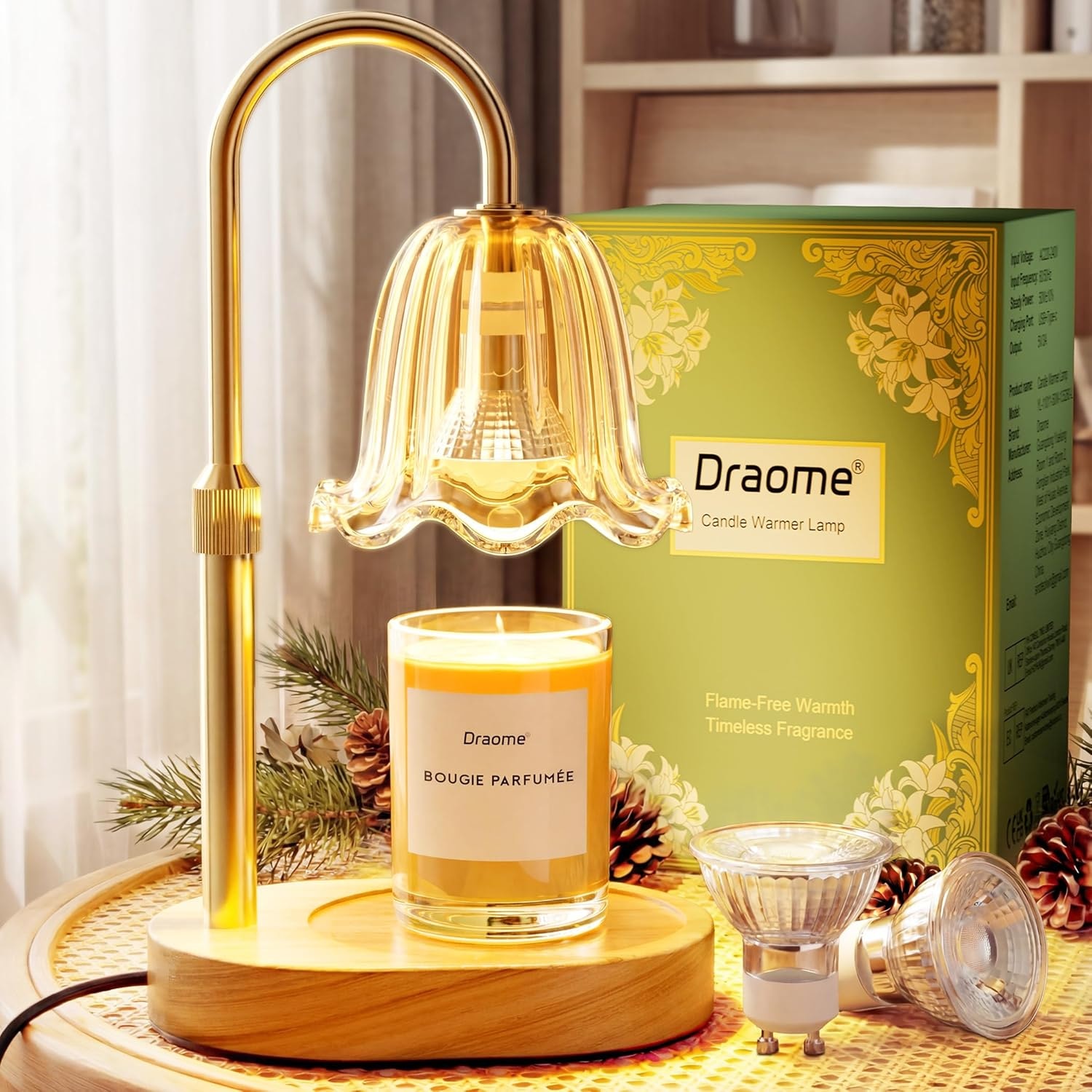 Gold flower candle warmer lamp lit over a jar candle beside its green Draome gift box and two spare bulbs