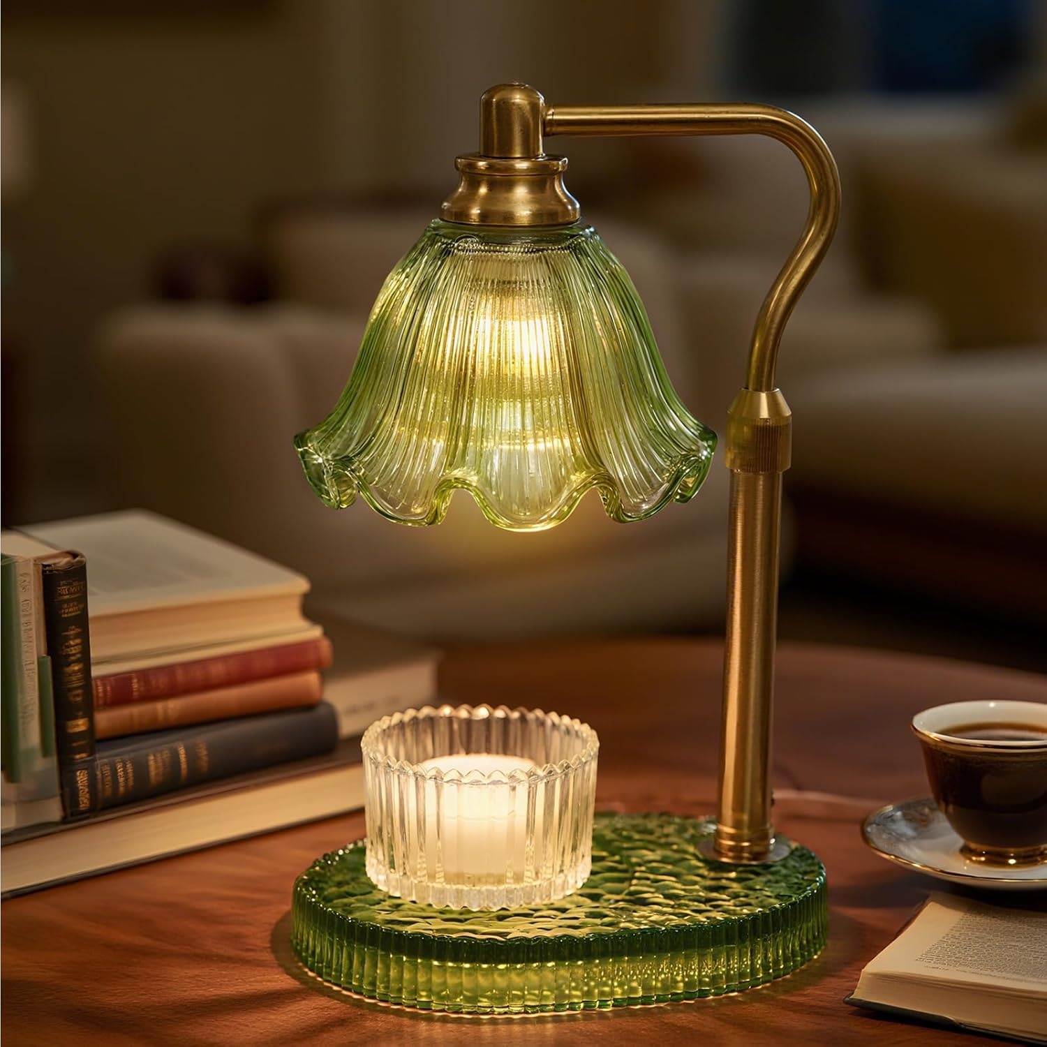 Green pressed glass candle warmer lamp lit above a jar candle beside stacked books and a cup of coffee
