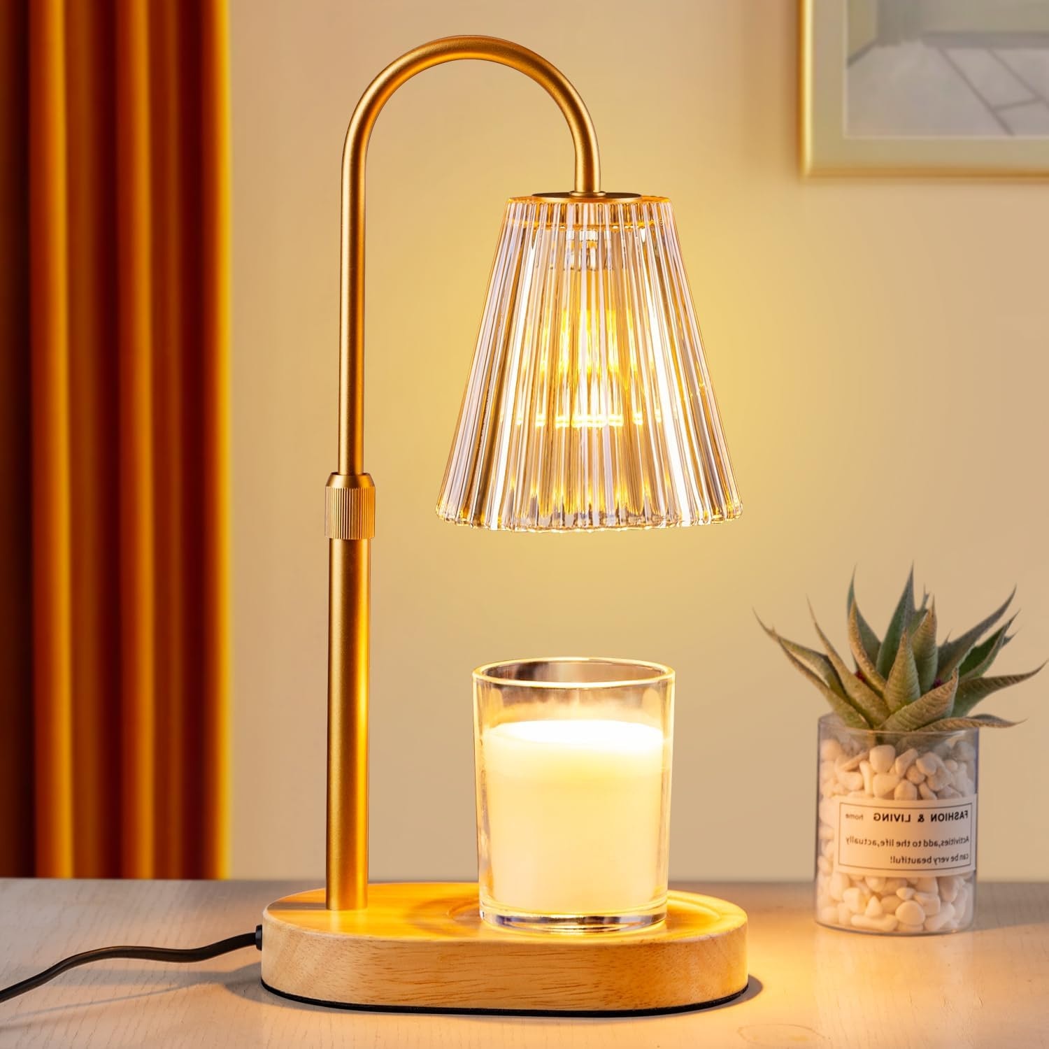Amber ribbed candle warmer lamp lit above a jar candle on a wooden table beside a small plant